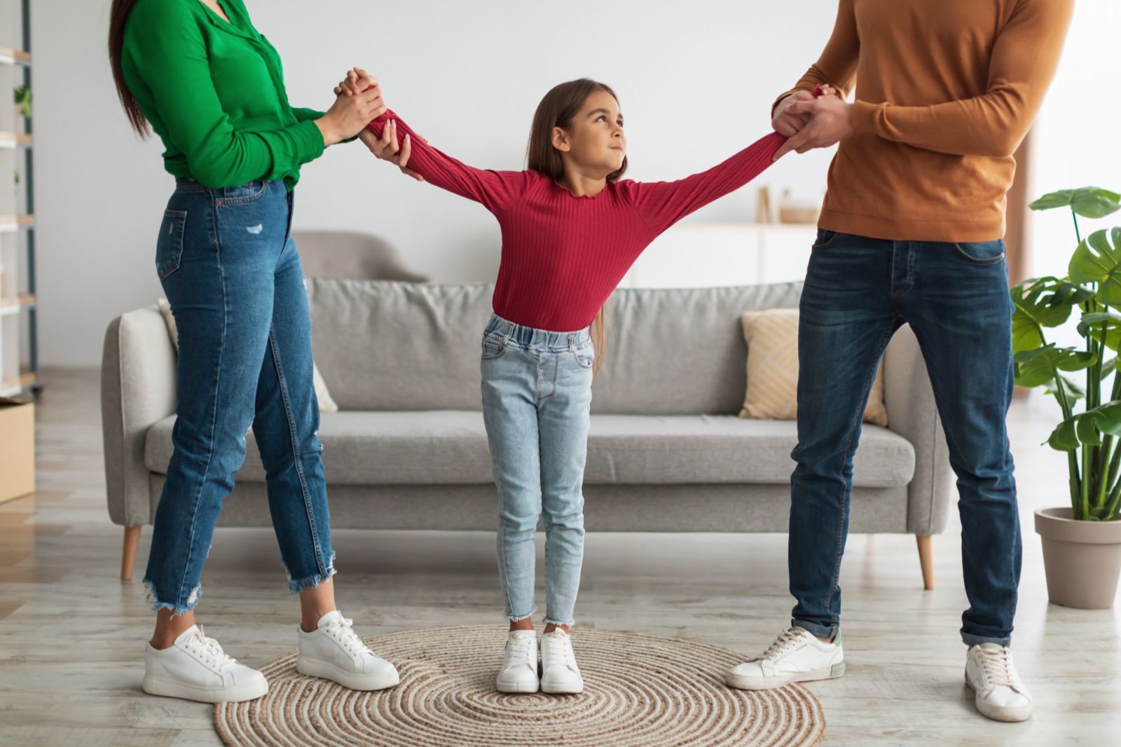 A child being pulled by the arms between her two parents in a living room