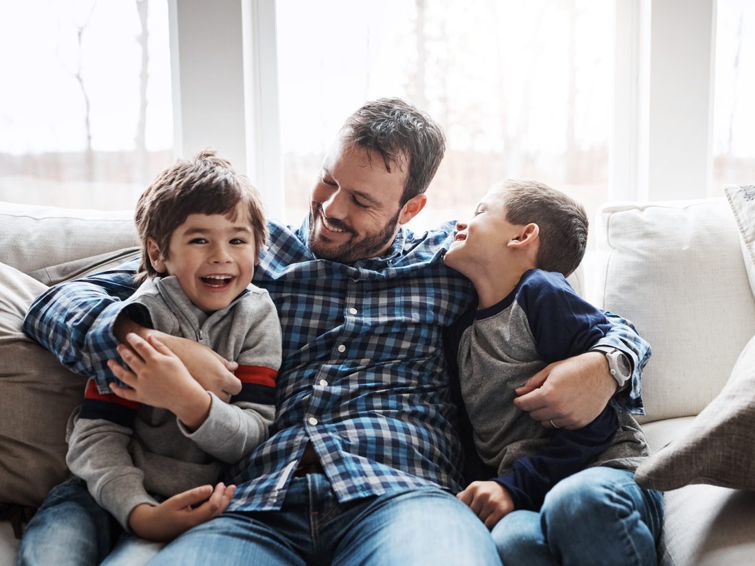 A father laughing with his two sons on the couch at home