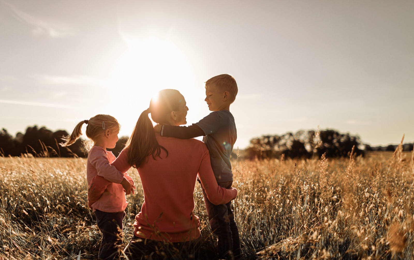 A parent in a field at sunset with two children