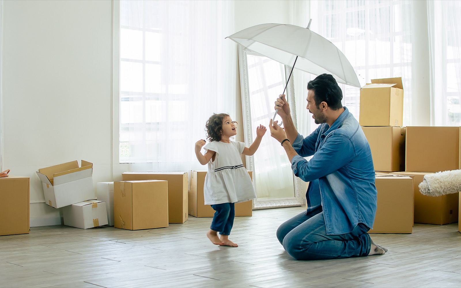 A father holding an umbrella over his young daughter among moving boxes in a new home