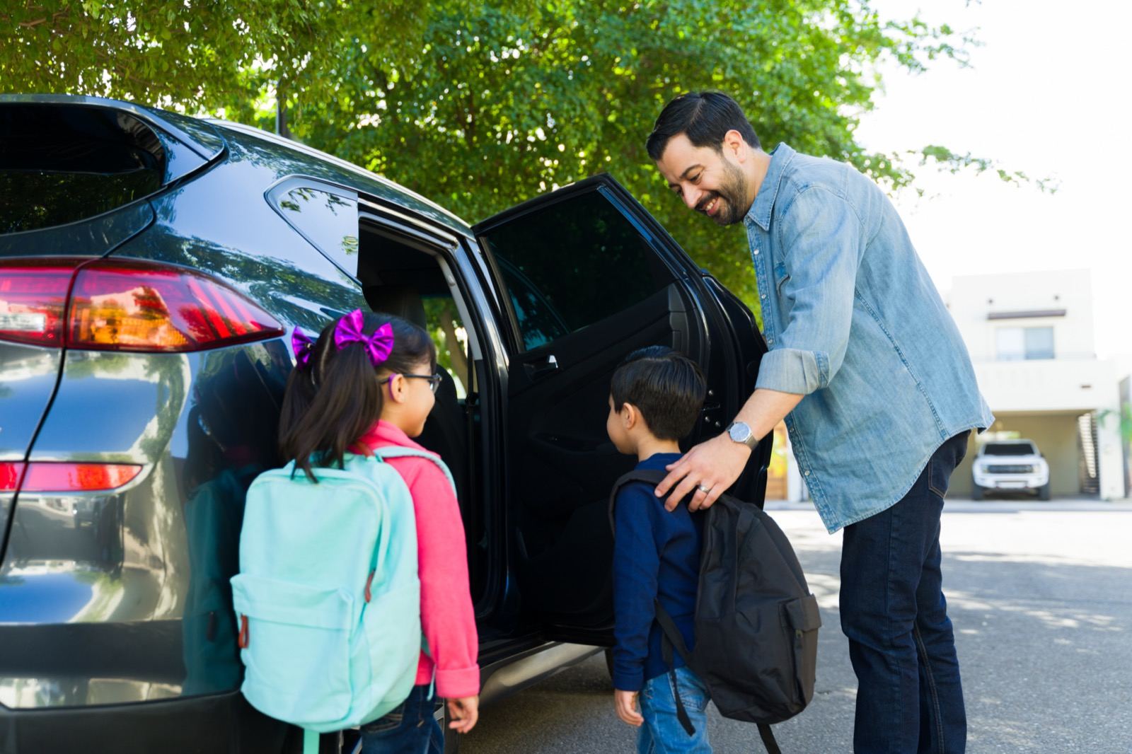 A father seeing his two children with backpacks into the car