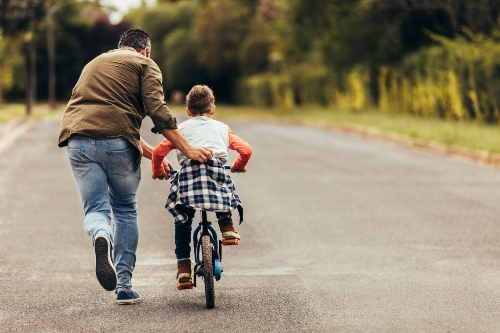 A father running alongside his son as he learns to ride a bike