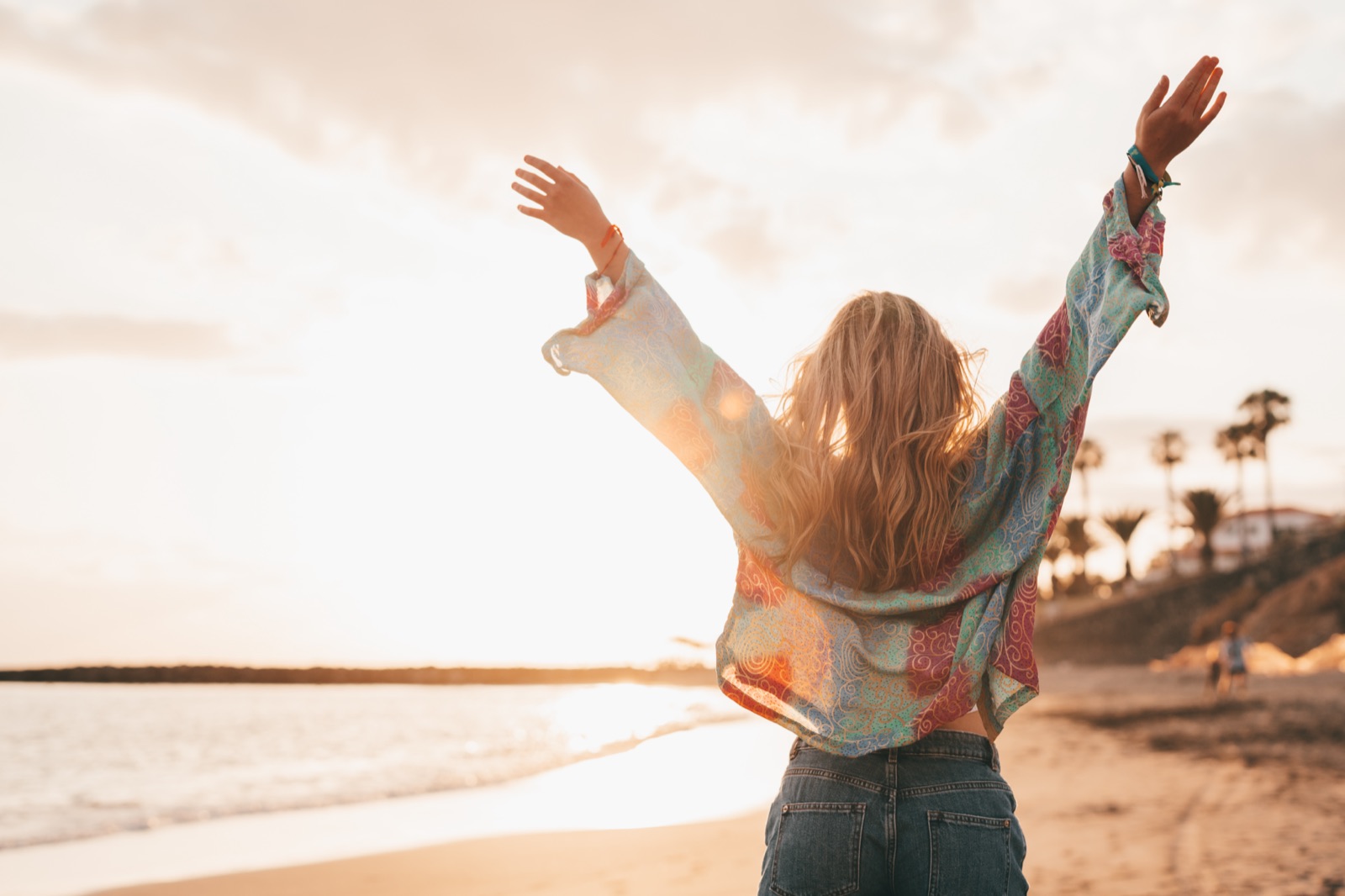 A woman on the beach at sunset, arms raised to the sky